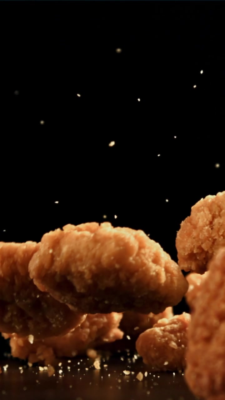 Crocchette di pollo fritte dorate che cadono in slow motion su sfondo nero