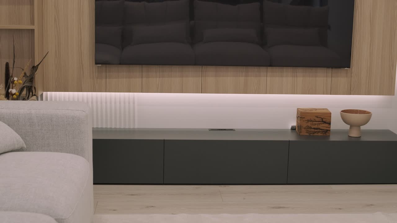A modern living room with a sleek entertainment unit, complemented by ambient lighting and stylish decor including a wooden box and a ceramic bowl, exudes sophistication and minimalism