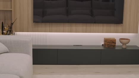una sala de estar moderna con una elegante unidad de entretenimiento, complementada por iluminación ambiental y una decoración elegante que incluye una caja de madera y un cuenco de cerámica, exuda sofisticación y minimalismo