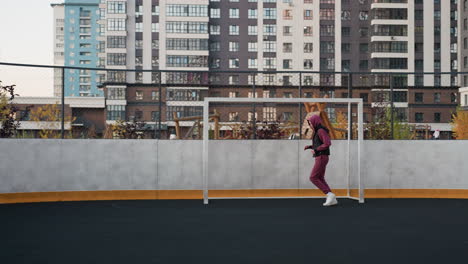 female jogger wearing hoodie vest and joggers sneakers runs around circular outdoor sports court marked by white post under modern apartment building facades at dusk in urban setting