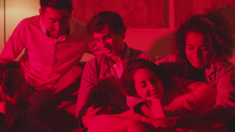 Group-of-friends-sitting-together-on-sofa-in-room-with-red-light