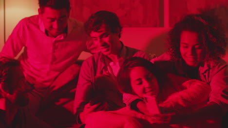 group of friends sitting together on sofa in room with red light