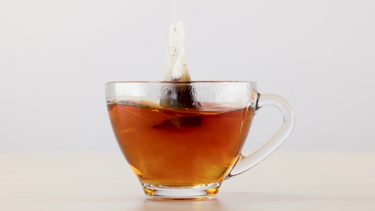 Primo piano di una bustina di tè in infusione in una tazza di vetro trasparente su sfondo bianco