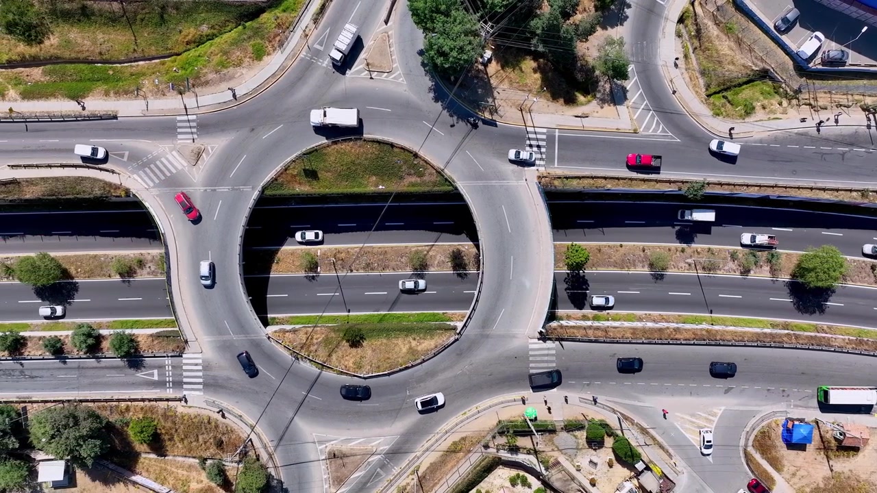 Top down dolly aerial shot over urban roundabout overpass with cars flowing through circular ring road above busy highway underpass with crosswalks and surrounding streets