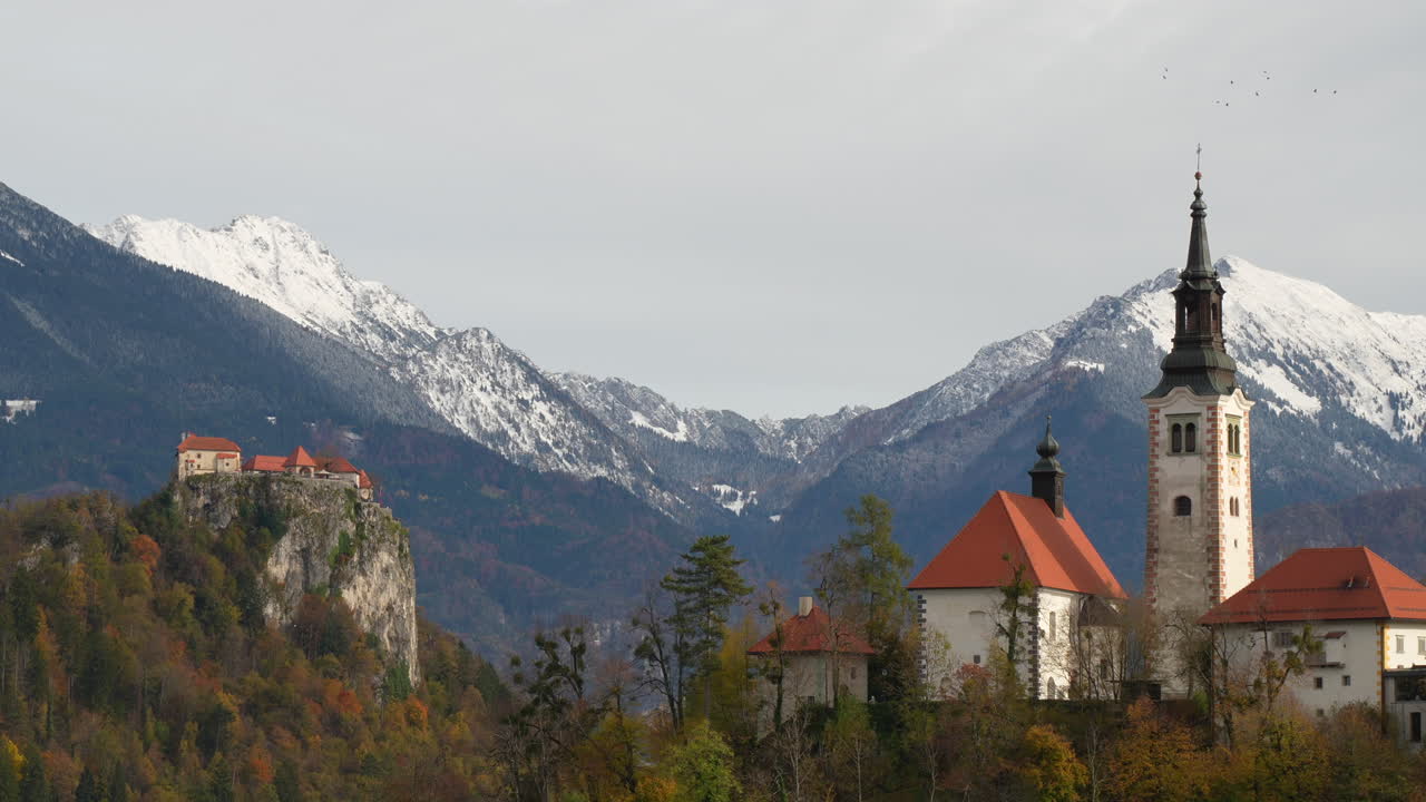 Bled Castle on a cliff and St. Martin's Parish Church with the snowy Julian Alps in Slovenia