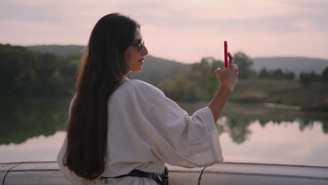 mujer tomando una foto al atardecer junto al lago