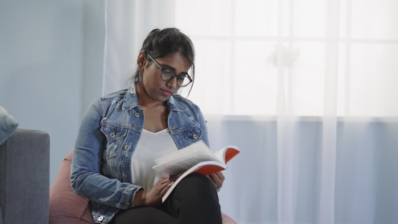 Focused Indian reader flips pages of book sitting on chair