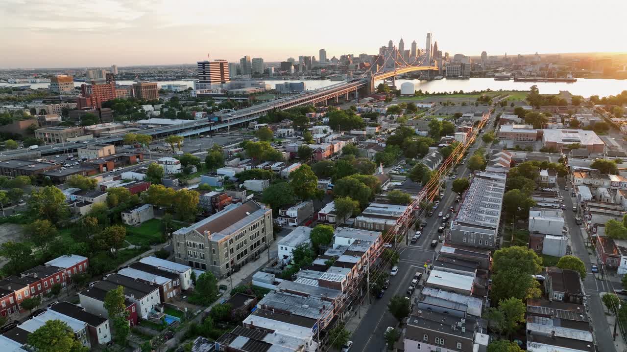 Suburb neighborhood of Camden in NJ and famous Benjamin Franklin Bridge Plaza at sunset. Cars crossing Delaware River and arriving Philadelphia, PA, America. Aerial rising wide shot
