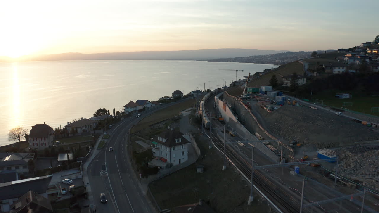 Aerial of train driving past highway near beautiful lake