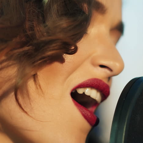 profile of a beautiful girl's face with perfect makeup singing in the sound studio. young singer emotionally recording new song. lady sings into microphone. slow motion close-up