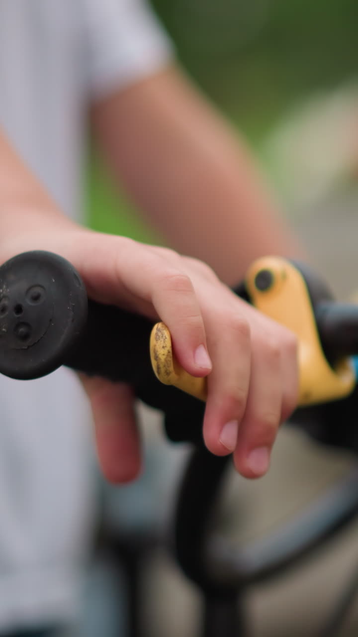 un primer plano de la mano de un niño agarrando el freno de una bicicleta mientras lleva una tapa blanca, con una vista de fondo borrosa