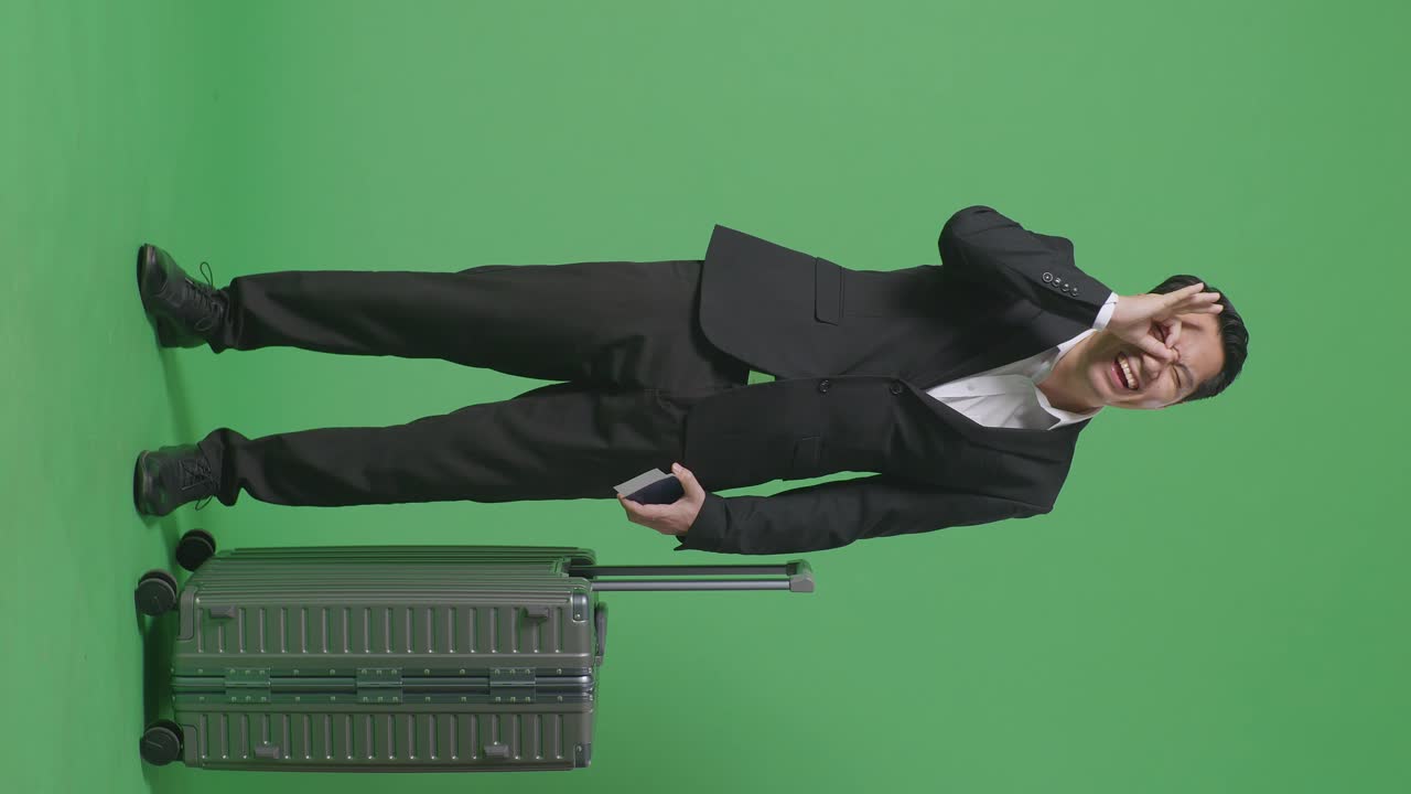 짐과 여권을 가진 아시아 사업가 여행자의 몸이 가득 차 있으며, 녹색 스크린 배경 스튜디오에 서있는 동안 눈 위에 ok 손 표시를 보여주고 미소 짓고 있습니다.