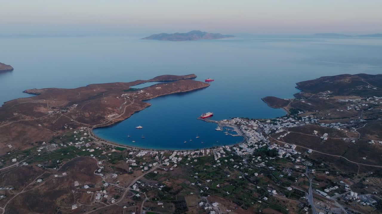 Drone establishing of Serifos port and Livadi village with calm Aegean sea during warm evening light