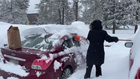 girl shoveling deep snow off of a car