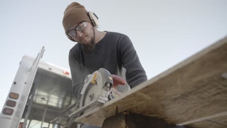 low angle view of carpenter cutting wooden board with electric circular saw