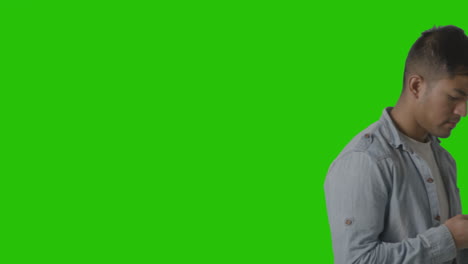 studio shot of casually dressed young man walking across frame messaging on mobile phone against green screen