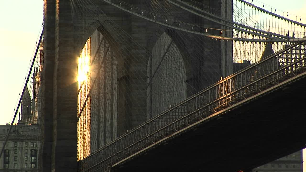 Gli archi gotici del Ponte di Brooklyn catturano appena la luce riflessa da un edificio in lontananza.