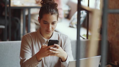 joven mujer de negocios enviando mensajes de texto en su teléfono inteligente en un café