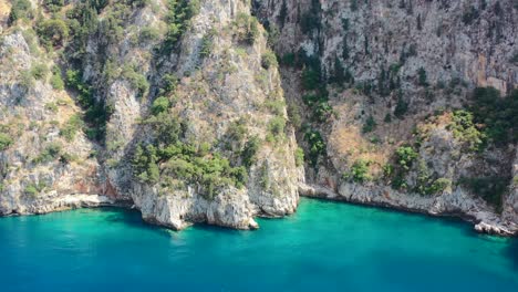 aerial drone approaching a beautiful turquoise blue ocean bay near butterfly valley in fethiye turkey surrounded with green mountain cliffs on a sunny summer day