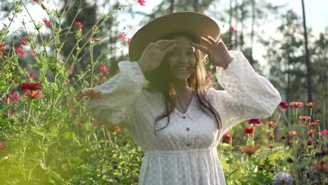 niña en un campo de flores, con sombrero y vestido blanco, sonriendo muy feliz durante la puesta de sol