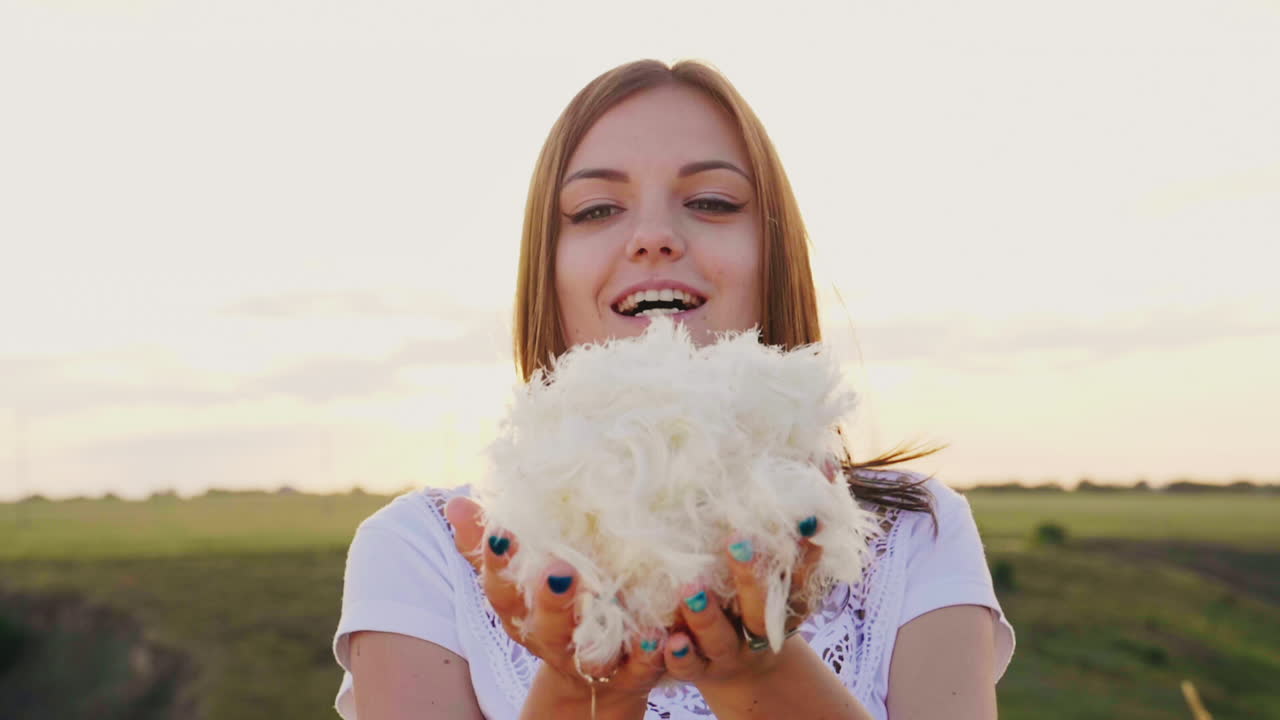 una mujer joven está jugando con una luz suave hacia abajo sopla sobre un montón de plumas que vuelan en forma directa
