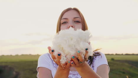 a young woman is playing with a gentle light down blows on a pile of feathers they fly in all direct