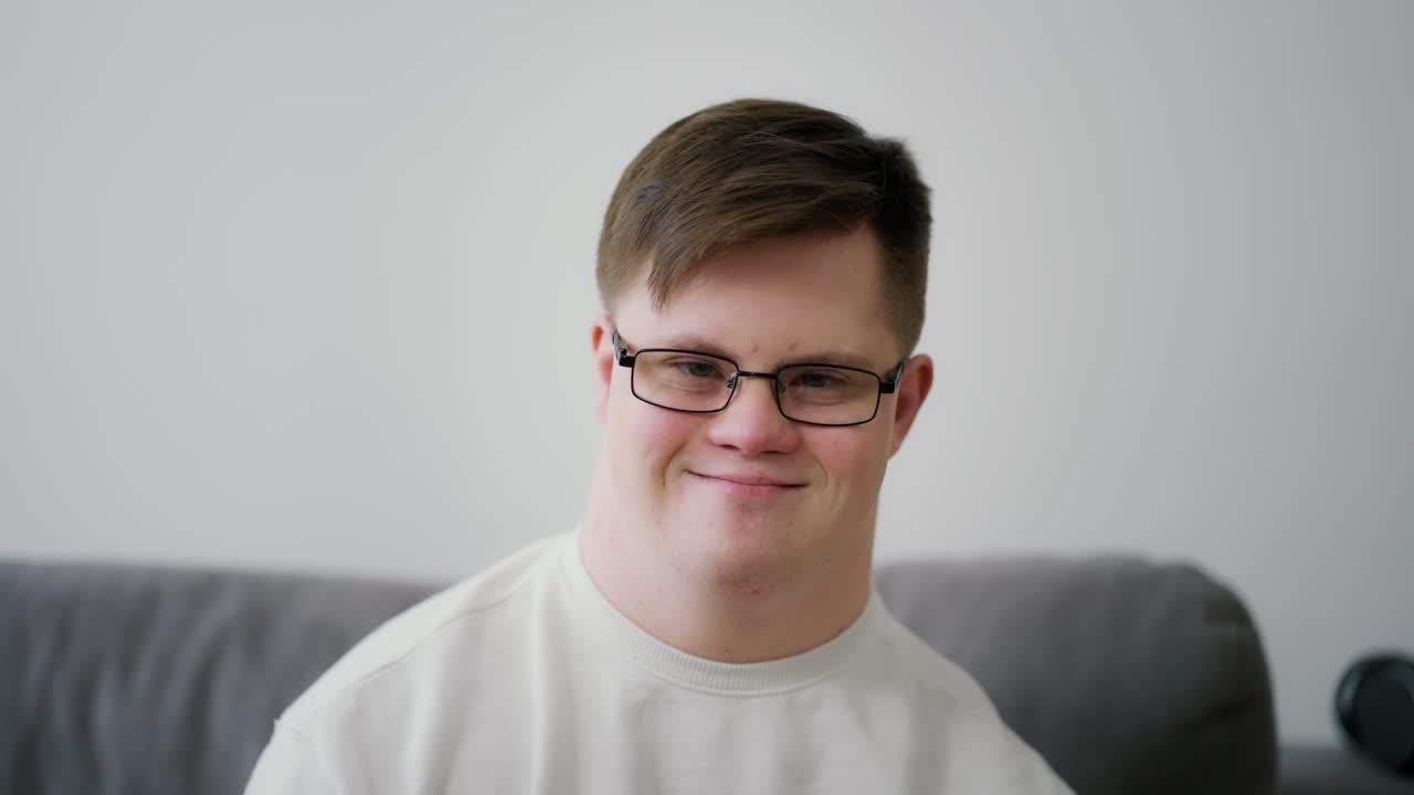 Jovem gentil com síndrome de Down sentado no sofá.