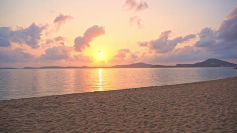 Una-Vista-Desde-La-Playa-De-Un-Paisaje-Nuboso-Que-Se-Forma-Alrededor-De-Las-Montañas-Que-Refleja-El-Sol-Tropical-Rosado,-Morado-Y-Amarillo