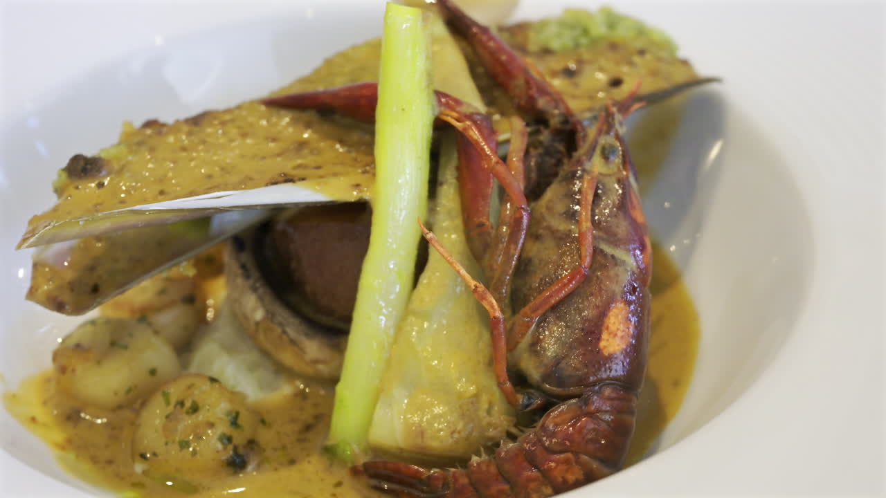 Close up of whole cooked crayfish with a mussel shell filled and a creamy herb topping on a white plate