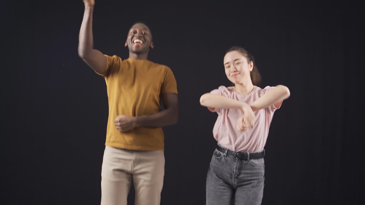 un hombre afroamericano y una joven asiática bailando y felices.
