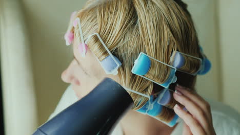 mujer con rulos en la cabeza seca el cabello con un primer plano de secador de pelo