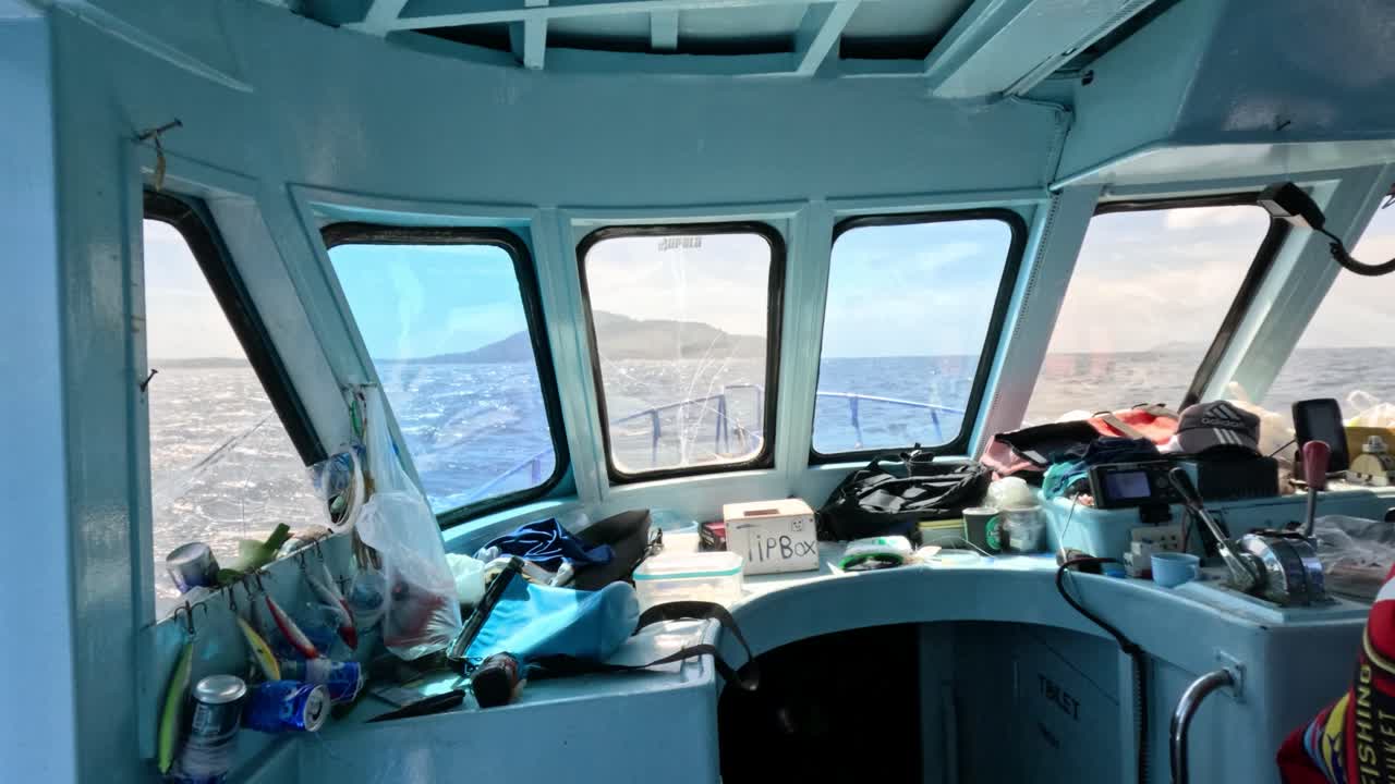 Camera moves through window into cluttered boat cabin, revealing ocean and coastline in daylight