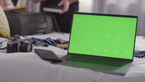 green screen laptop with person packing suitcase on bed at home for summer holiday 2