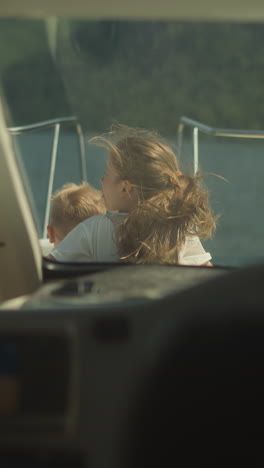 girl with ponytail and little boy take sunbathe on sailboat bow deck view from skipper cockpit. calm children enjoy seascape riding yacht on vacation