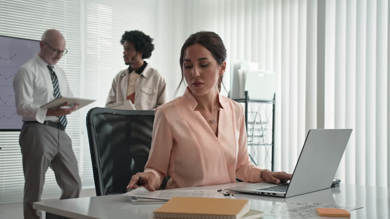 Female Project Manager Working on Laptop when Colleagues Talking in Background