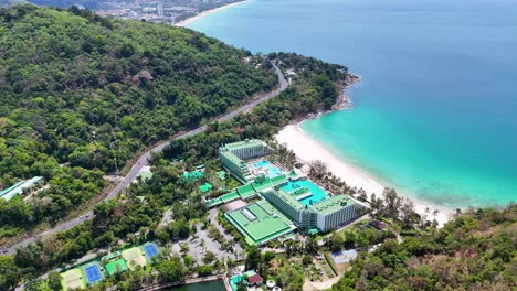 drone footage captures a luxury beachfront resort in phuket, thailand, showcasing vibrant turquoise waters and lush greenery under bright daylight