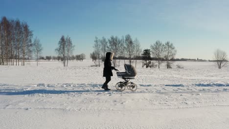 Frau-Im-Dunklen-Wintermantel-Spaziert-Mit-Kinderwagen-Auf-Verschneiter-Landstraße