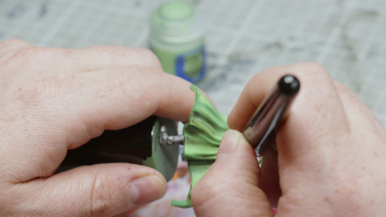 artista cepillando suavemente pintura de color verde en el modelo de fantasía en su estudio de taller con olla de pintura verde y mesa en el fondo 4k