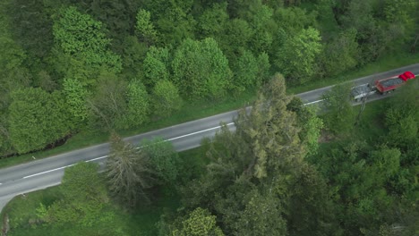 un camión y un remolque cargado de grava, conduciendo a través del bosque en una carretera de asfalto