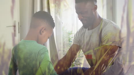 animation of grass over happy african american father and son dressing up together