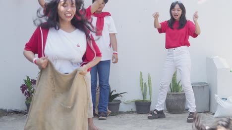 young asian woman pushing and cheat during sack race celebrating indonesian independence day, august 17