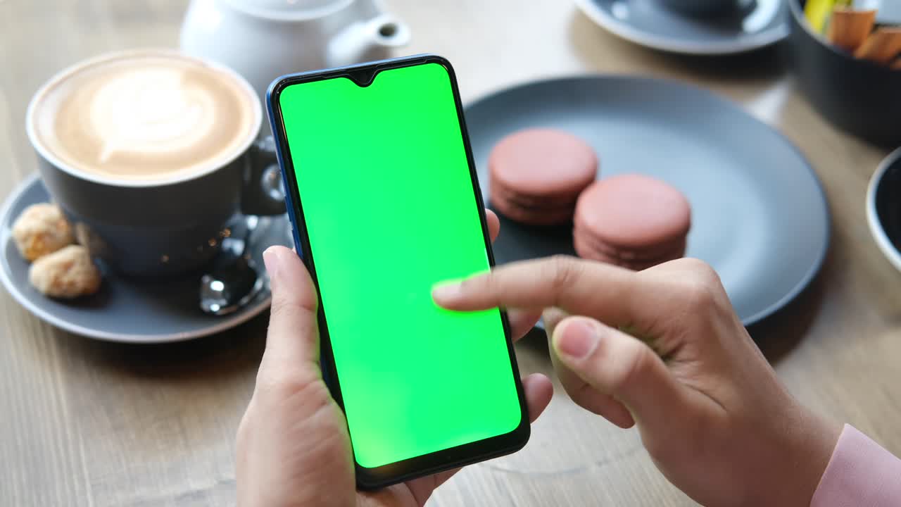 persona usando un teléfono inteligente con pantalla verde en una cafetería