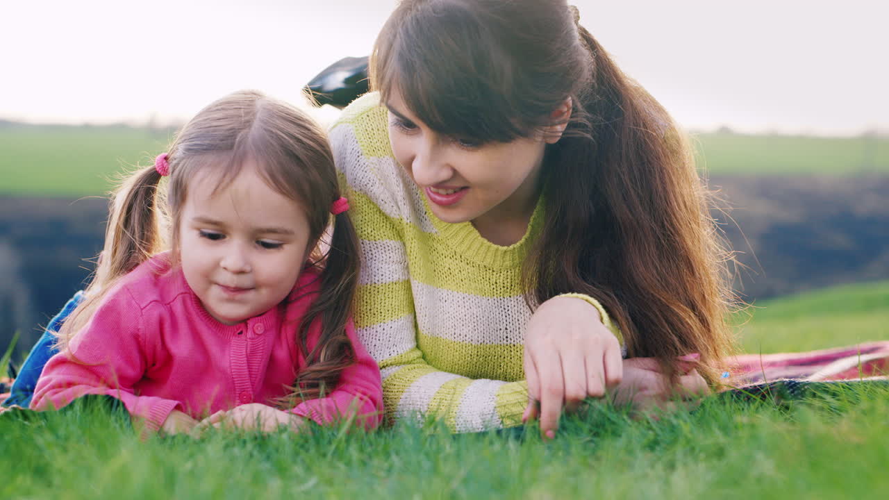feliz madre y su hija disfrutan de la naturaleza examinando cuidadosamente la hierba verde y la primera primavera