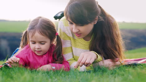 feliz madre y su hija disfrutan de la naturaleza examinando cuidadosamente la hierba verde y la primera primavera