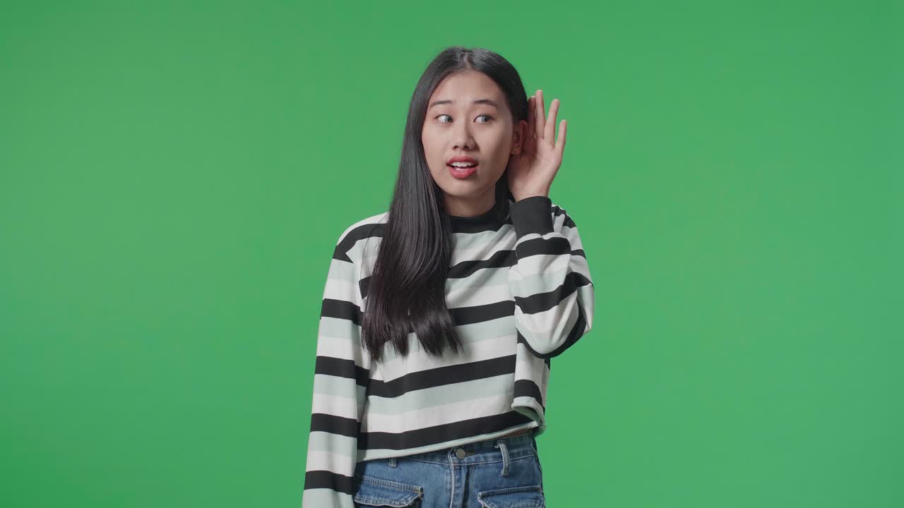 Persona asiatica che ascolta attentamente qualcosa in piedi davanti a uno sfondo green screen