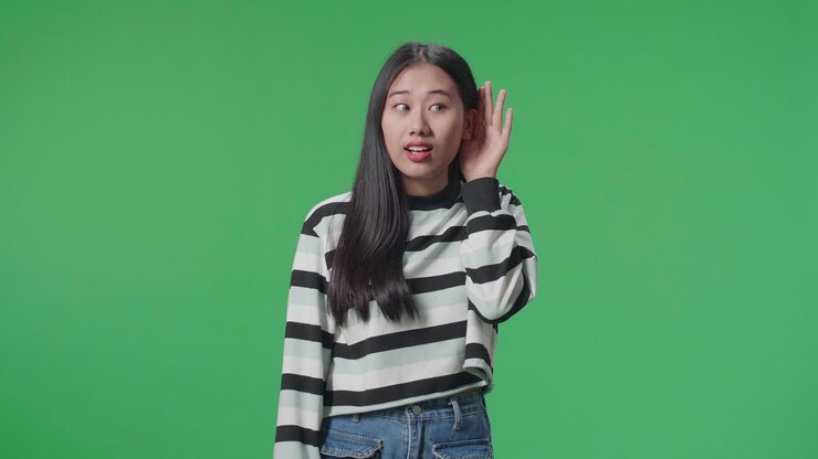 Persona asiatica che ascolta attentamente qualcosa in piedi davanti a uno sfondo green screen