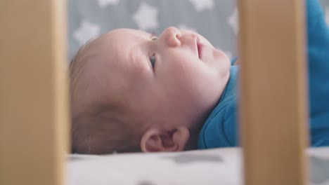 cute-baby-with-blue-eyes-touches-face-with-fist-in-cot