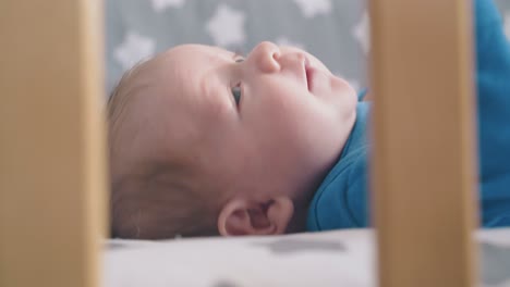 un bebé lindo con ojos azules toca la cara con el puño en la cuna