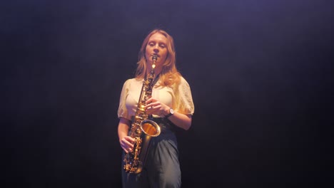 Joven-Mujer-Caucásica-Tocando-Solo-En-Saxofón-Bajo-Luces-De-Escenario-En-Neblina