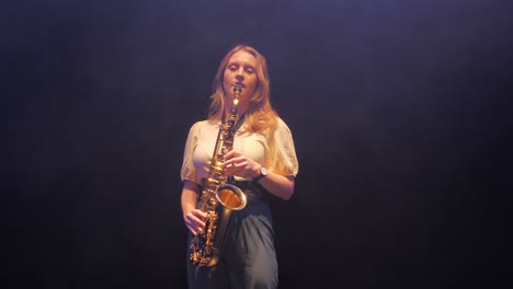 joven mujer caucásica tocando solo en saxofón bajo luces de escenario en neblina